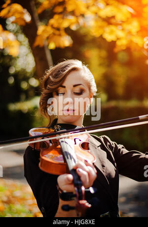 Portrait de jeune fille intelligente avec violon sur les mains en plein air sur la couche brune de l'automne. Banque D'Images