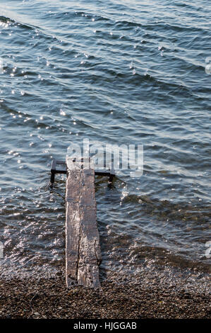 Dock en bois humide s'avançant dans le gris bleu des eaux du lac Baikal d'une plage de galets. Les petites vagues reflètent les rayons du soleil.Lake Banque D'Images