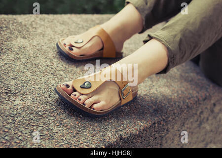 Pieds de femme en jaune foncé avec des sandales d'été élégant vernis à ongles, en pantalon d'été vert assis sur le mur Banque D'Images