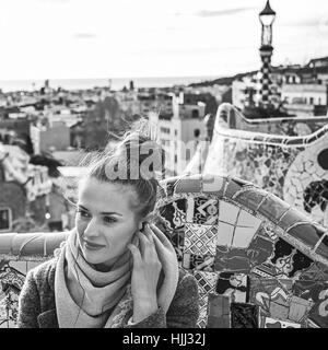 Style signature de Barcelone. Jeune femme manteau en tourisme à Barcelone, Espagne audioguide écoute alors que assis sur un banc Banque D'Images