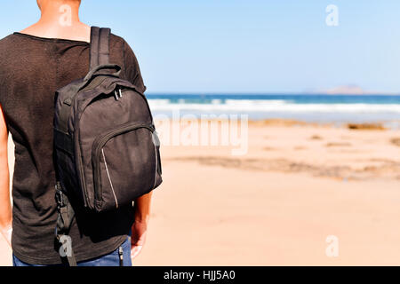 Libre d'un jeune homme de race blanche vu de dos portant un t-shirt et de transporter un sac à dos, debout sur une plage de sable blanc Banque D'Images