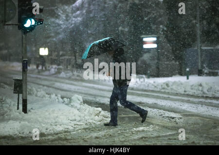 Un homme avec parapluie traverser la route au passage piéton, le tableau de bord au cours de fortes chutes de neige dans la région de Zagreb, Croatie. Banque D'Images