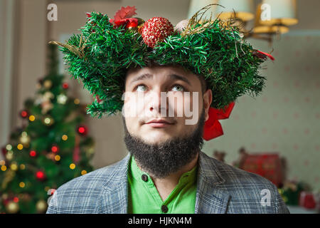 Homme barbu en T-shirt vert et une veste avec une couronne de Noël sur la tête Banque D'Images