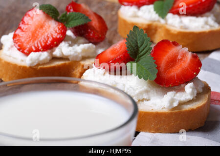 Des sandwichs avec du fromage à pâte molle et de fraises fraîches et un verre de lait à l'avant-plan. petit déjeuner vitamine Banque D'Images