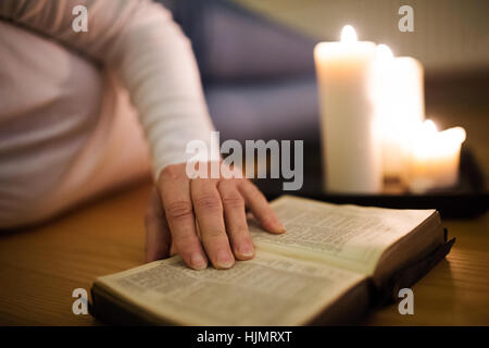 Méconnaissable woman reading Bible. Brûler des bougies à côté d'elle. Banque D'Images