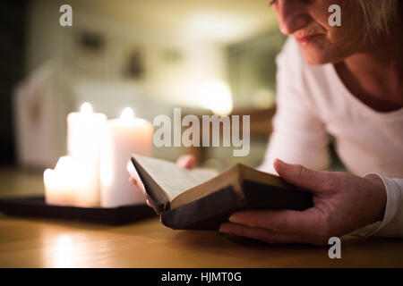 Méconnaissable woman reading Bible. Brûler des bougies à côté d'elle. Banque D'Images