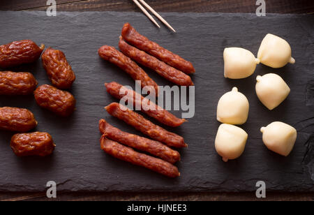 Mini saucisses séché et fumé et fromage sur la plaque en pierre d'ardoise noire Banque D'Images