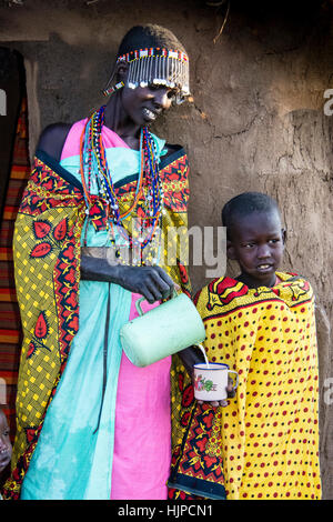 Masaï verser le lait pour un enfant, portant des vêtements traditionnels, dans un village proche de Parc National du Masai Mara, Kenya, Afrique de l'Est Banque D'Images