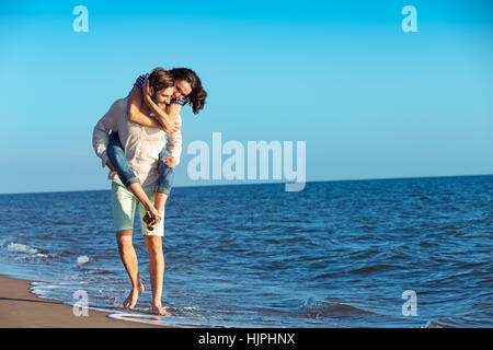 Bel homme piggy back donnant à sa petite amie à la plage Banque D'Images