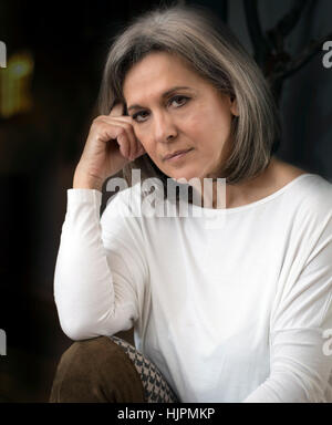 Femme mature à la recherche de sérieux, de réflexion, de bras sur le genou, la main sur la joue. Banque D'Images