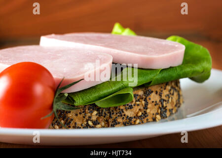 Sandwich ouvert avec jambon, salade verte et tomates sur une plaque blanche Banque D'Images