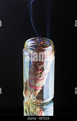 Paquet de barbouiller ou sage comme encens brûlant en pot sur fond noir. Banque D'Images