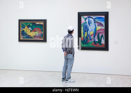 Visiteur en face de la peintures vaches rouge, vert, jaune (1912) et Blue Horse I (1911) par peintre expressionniste allemand Franz Marc affiché dans la galerie Lenbachhaus à Munich, Bavière, Allemagne. Banque D'Images