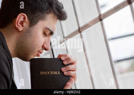 Young man holding Bible et prier par fenêtre Banque D'Images