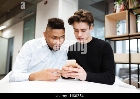 Photo de deux professionnels étudiants assis dans la bibliothèque et l'utilisation de téléphone cellulaire. Banque D'Images