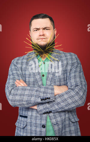 Homme barbu gras coincé dans sa barbe et spaghetti en colère sur fond rouge Banque D'Images