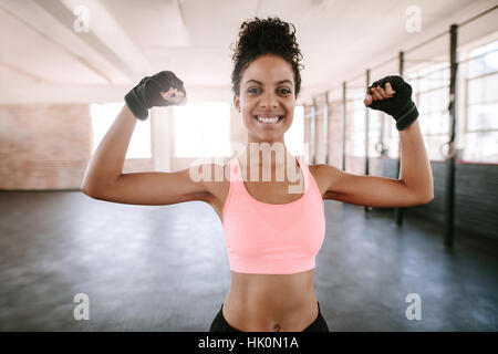Portrait of young woman flexing muscles et remise en forme de sourire. Modèle féminin en Afrique sportswear montrant ses muscles. Banque D'Images