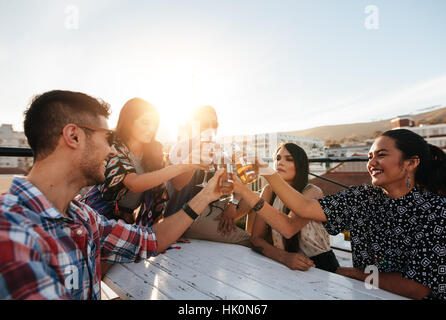 Groupe de jeunes toasting drinks lors d'une soirée sur le toit. Les jeunes bénéficiant d'amis avec des boissons. Banque D'Images