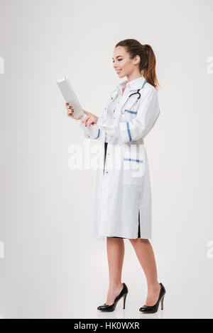 Toute la longueur de jeune femme médecin et permanent à l'aide de tablet over white background Banque D'Images