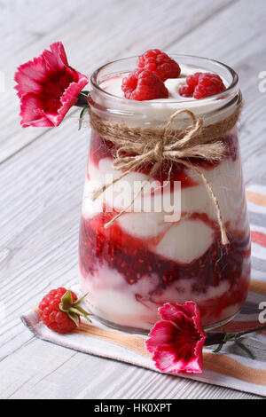 Dessert avec lait framboises dans un pot en verre décoré de fleurs gros plan sur une table en bois vertical. Banque D'Images