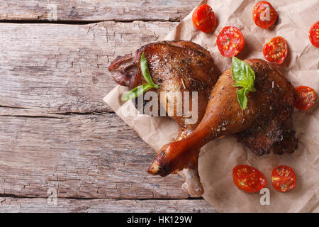 Deux cuisses de canard rôti avec tomates et basilic close up sur une vieille table horizontale Vue de dessus Banque D'Images