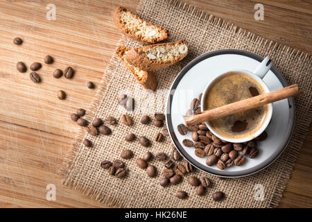Un studio, nature morte d'une tasse de café sur une soucoupe avec un bâton de cannelle, fèves grillées et des biscuits sur un tapis de jute Banque D'Images