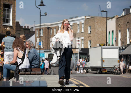 Londres, ANGLETERRE - 12 juillet, 2016 petite fille en rose à la mode des lunettes de parler au téléphone, marcher dans la rue Broadway Road Banque D'Images