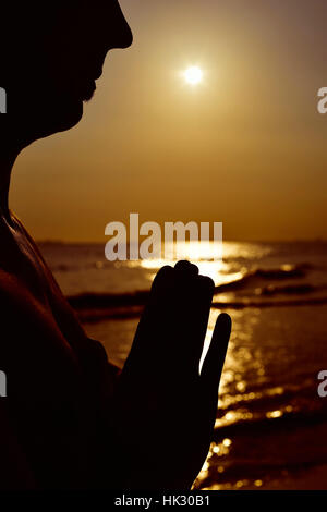 La silhouette d'un jeune homme avec ses mains mis ensemble en faisant levier au bord de la mer à rétro-éclairage Banque D'Images