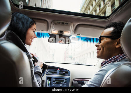 Une jeune femme et jeune homme dans une voiture à l'un l'autre et souriant, vu depuis le siège arrière. Banque D'Images