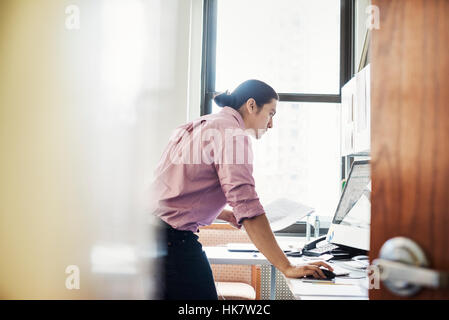 Un homme debout dans son bureau s'appuyant sur le bureau, vue à travers une porte ouverte. Banque D'Images
