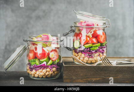 Déjeuner à emporter en bonne santé. Les légumes et les germes de pois chiches salade vegan dans des bocaux en verre, mur de béton gris, l'arrière-plan copie espace, selective focus. Cle Banque D'Images