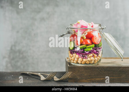 Déjeuner à emporter en bonne santé jar. Les légumes et les germes de pois chiches salade vegan en bocal en verre, mur de béton gris, l'arrière-plan copie espace, selective focus. Nettoyer Banque D'Images