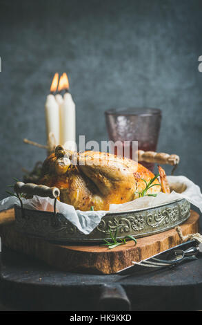 Set de table de Noël avec un poulet entier rôti à l'orange, boulgour et romarin, bougies décoratives, verre de vin rose, mur de béton gris backgroun Banque D'Images