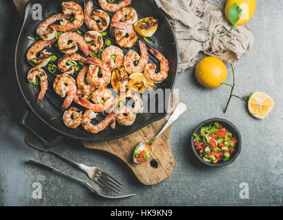 Dîner de fruits de mer. Crevettes géantes grillées sur le gril en fonte poêle avec citron, poireau, piment et sauce salsa menthe sur fond de béton gris, haut Banque D'Images