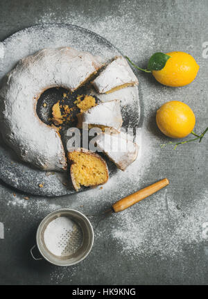 Des plats sans gluten gâteau bundt de citron avec du sucre en poudre servi avec des citrons fraîchement cueillies sur fond de béton gris, vue du dessus, vertical compositio Banque D'Images