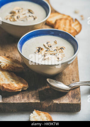 Dîner sain avec sauce crémeuse aux champignons soupe dans des bols et de tranches de pain grillées sur servant plus rustique conseil gris en arrière-plan, selective focus Banque D'Images