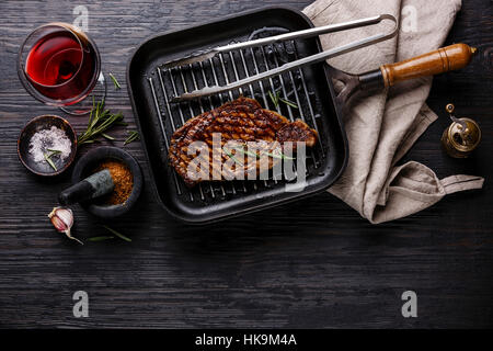 Faux filet entrecôte grillée sur pan et vin rouge sur fond de bois brûlé noir copy space Banque D'Images