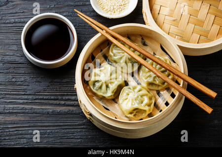 Boulettes à la vapeur Dim Sum en bateau à vapeur de bambou noir sur fond de bois brûlé Banque D'Images