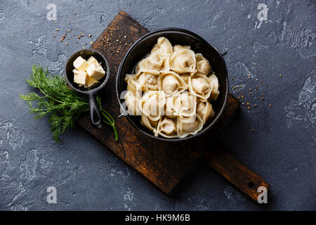 Beignets de viande des pelmeni russes avec du beurre en pot de fer noir sur fond noir en sombre Banque D'Images