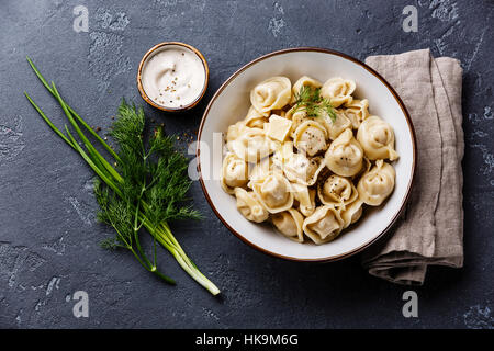 Beignets de viande des pelmeni russes avec la sauce à la crème sure et verts au bol sur pierre sombre contexte Banque D'Images