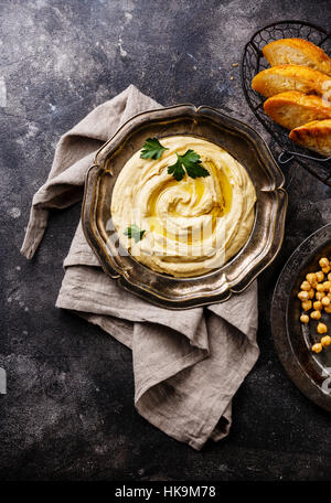 Houmous fait maison avec des toasts de pain dans la plaque en métal sur fond noir en noir Banque D'Images