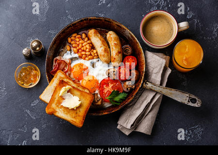 Petit-déjeuner anglais dans la casserole avec les œufs, saucisses, bacon, haricots, des toasts et du café à l'arrière-plan en pierre sombre Banque D'Images