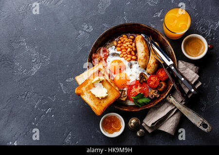 Petit-déjeuner anglais dans la casserole avec les œufs, saucisses, bacon, haricots, toasts et café sur pierre sombre contexte copy space Banque D'Images