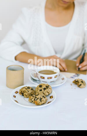 Une femme écrit une lettre en s'oatmal les cookies et café. Banque D'Images