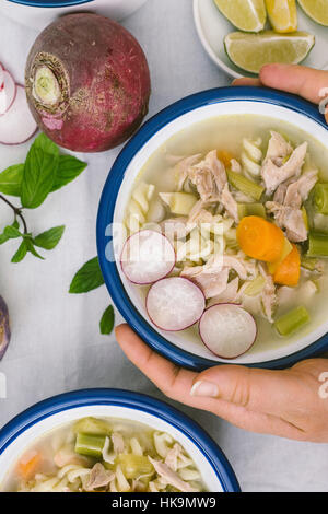 Mains tenant un bol de soupe au poulet avec des pâtes, de poireau et de carotte. Banque D'Images