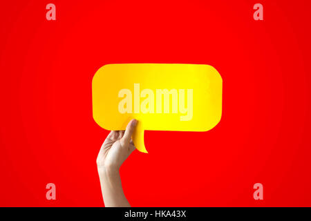 La main de l'Holding Speech Bubble jaune sur fond rouge - ballon bulle concept Banque D'Images