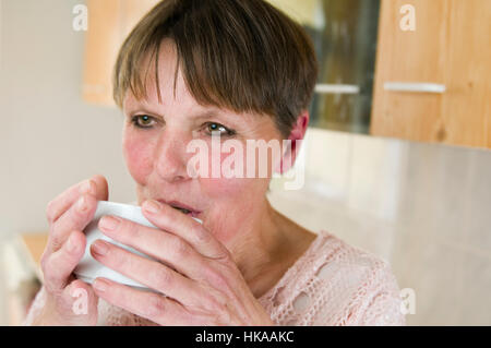 Tête et épaules latérales portrait d'une femme âgée d'une tasse blanche dans l'environnement domestique. Banque D'Images