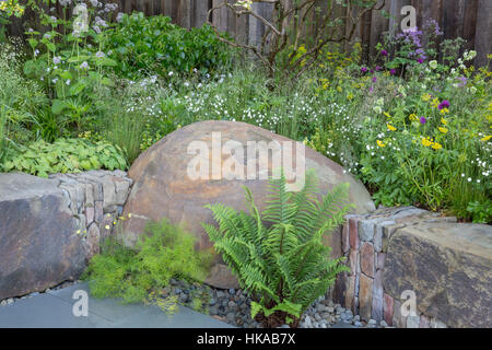 petit jardin à l'arrière avec parterres de fleurs surélevés avec de grands bancs en pierre rocheux plantes de plantation de printemps fougères uk Banque D'Images