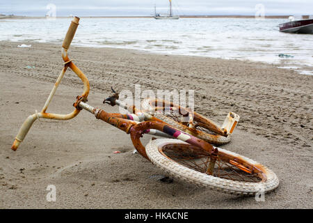Vélo pour enfants sur une plage avec bateau à voile à l'arrière-plan, Gjoa Haven, au Nunavut, Canada Banque D'Images