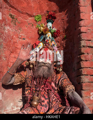 Saint homme ou au Népal Katmandou Pashupatinath sadhus. Le mans face est peinte en rouge et blanc qu'il a un couvre-chef et fait un geste avec sa main. Banque D'Images